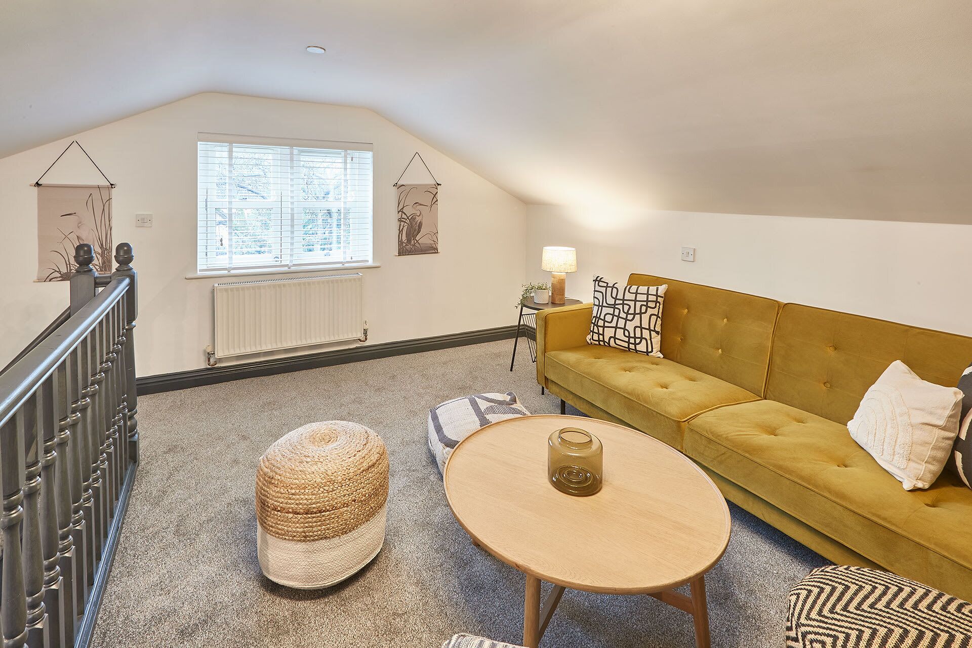 Ein gemütliches Schlafzimmer im Loft-Stil mit einem gelben Sofa, einem runden Holztisch und einem gewebten Pouf.