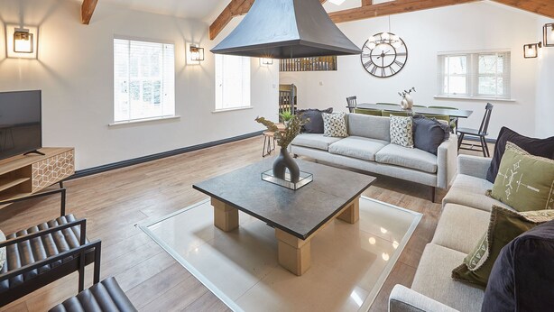 Un salon spacieux avec un plafond haut, des poutres en bois, une grande fenêtre, un canapé, une table basse et un téléviseur.
