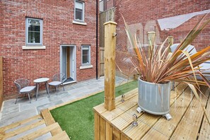Un bâtiment en briques doté d’un petit patio, comprenant une terrasse en bois, un pot de fleurs et des sièges d’extérieur.