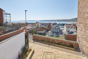 A residential area with a view of the sea, featuring brick buildings, a paved walkway, and a metal fence.