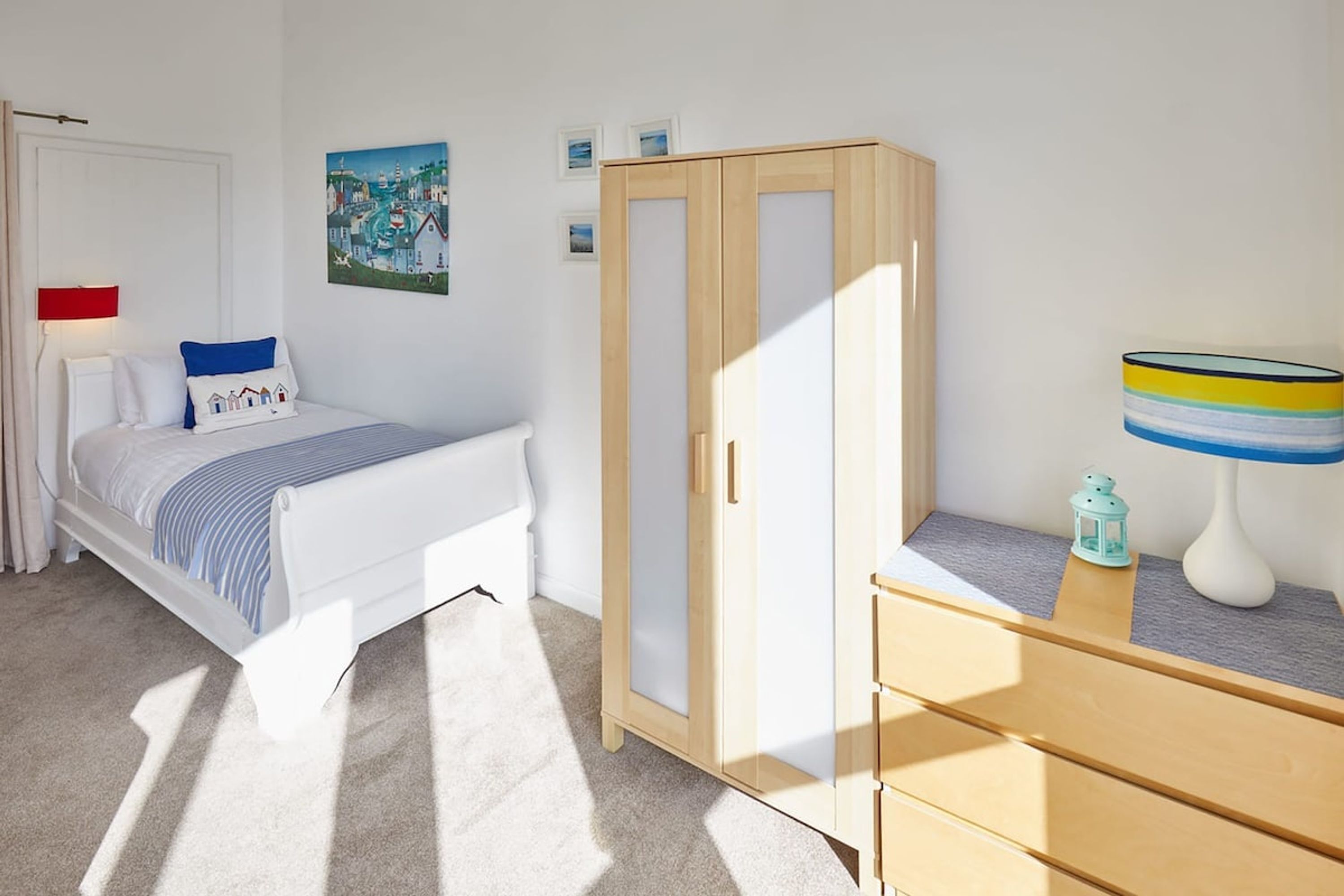 Une chambre à coucher avec un lit, une armoire, une commode, une lampe et un tableau au mur.