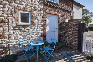 Cozy cottage with a traditional exterior, featuring a small table and two chairs in front of a white door.