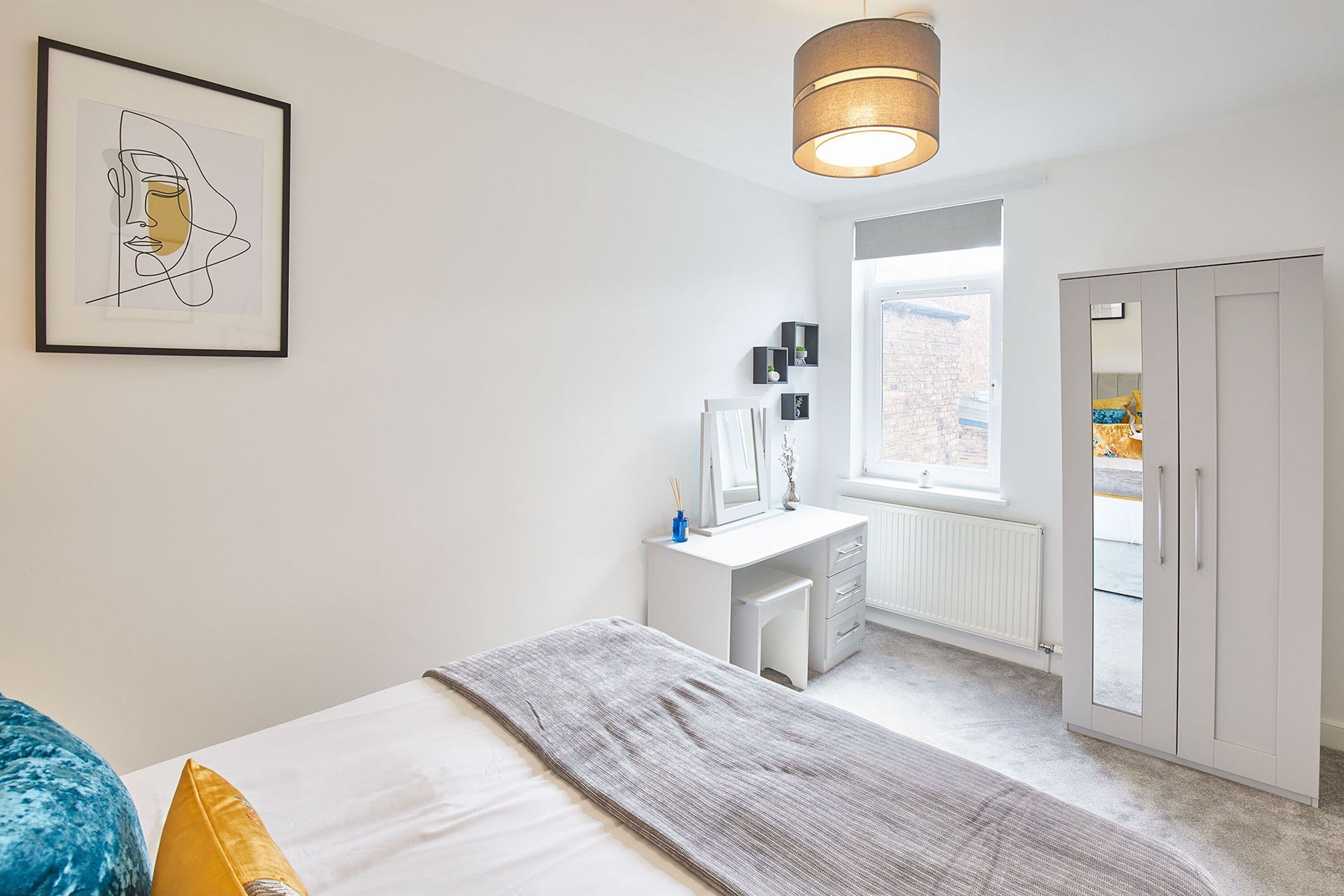 Een slaapkamer met een bed, nachtkastje, kledingkast en een kunstwerk in een lijst aan de muur.