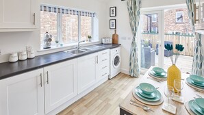 Una cocina moderna con armarios blancos, lavadora integrada y comedor con platos azul turquesa y amarillos.