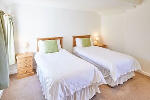 Two single beds with wooden headboards and white bedspreads, each with a bedside table and lamp.