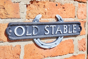 An old stable sign is mounted on a brick wall.