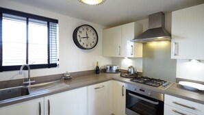 Een moderne keuken met witte kasten, een roestvrijstalen spoelbak, een gasfornuis en een wandklok.