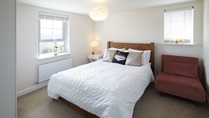 Een slaapkamer met een bed, nachtkastje, lamp, stoel en een raam met zonwering.