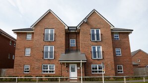 Een tweelaags bakstenen appartementencomplex met een centrale ingang, meerdere ramen en een klein portiek.