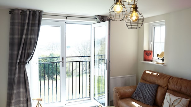 Een woonkamer met een bruine leren bank, een glazen salontafel en een groot raam met uitzicht op een balkon.