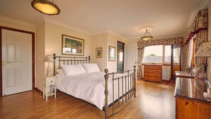 A bedroom with a wooden bed, a nightstand, a dresser, and a window with floral curtains. - Host Stay Cheviot View (Seahouses)