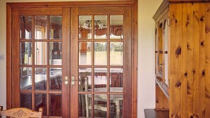 A wooden double door with glass panels, a wooden cabinet, and a chair. - Host Stay Cheviot View (Seahouses)