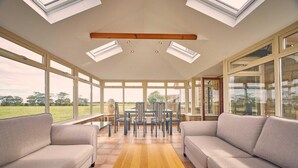 A spacious room with large windows, a wooden ceiling beam, and a central seating area with a table and chairs. - Host Stay Cheviot View (Seahouses)