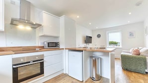 A modern kitchen with white cabinets, a built-in microwave, a stainless steel oven, and a compact dishwasher. - Host Stay Ocean Pearl (Seahouses)