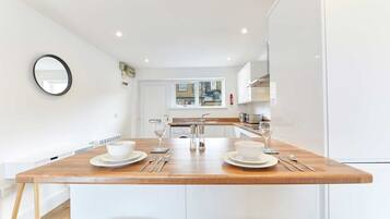 A modern kitchen with white cabinetry, a wooden island with two white bowls and wine glasses, and a window with a view of buildings.
