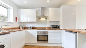 A compact kitchen with white cabinets, a stainless steel range hood, a microwave, a toaster, and a dishwasher. - Host Stay Ocean Pearl (Seahouses)