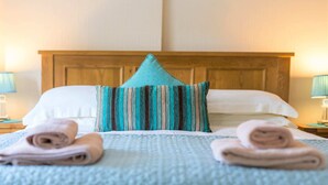Cama bem arrumada com travesseiro listrado, dois rolos de toalha e cabeceira de madeira.