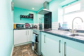 A kitchen with teal cabinets, a stainless steel sink, and a window above the sink. - Host Stay No 4 Daisy Cottage (Belford)