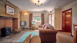 A living room with a brick fireplace, a sofa, a television, and a window with curtains. - Host Stay No 3 Rose Cottage (Belford)