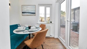 A dining area with a table set for four, a teal tablecloth, and brown chairs. There is a window with a view of the outside, and a painting on the wall. - Host Stay The Blacksmiths (Morpeth)