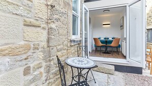 A stone exterior wall, a glass door leading to a dining area with a table and chairs, and a small outdoor seating area with a table and chairs. - Host Stay The Blacksmiths (Morpeth)