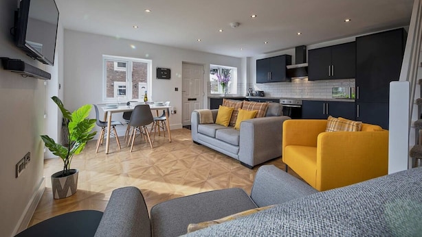 A modern living room with a sofa, armchairs, and a dining area with a table and chairs. - Host Stay The Bach (Chathill)