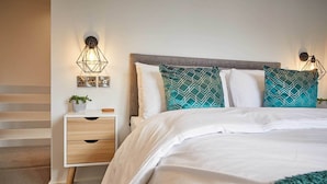 A bedroom with a bed, nightstands, a wall-mounted light fixture, and a potted plant. - Host Stay The Bach (Chathill)