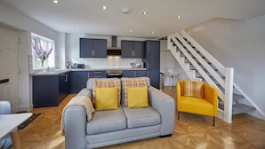 A modern kitchen with dark cabinets, a grey sofa with yellow cushions, and a yellow armchair. - Host Stay The Bach (Chathill)
