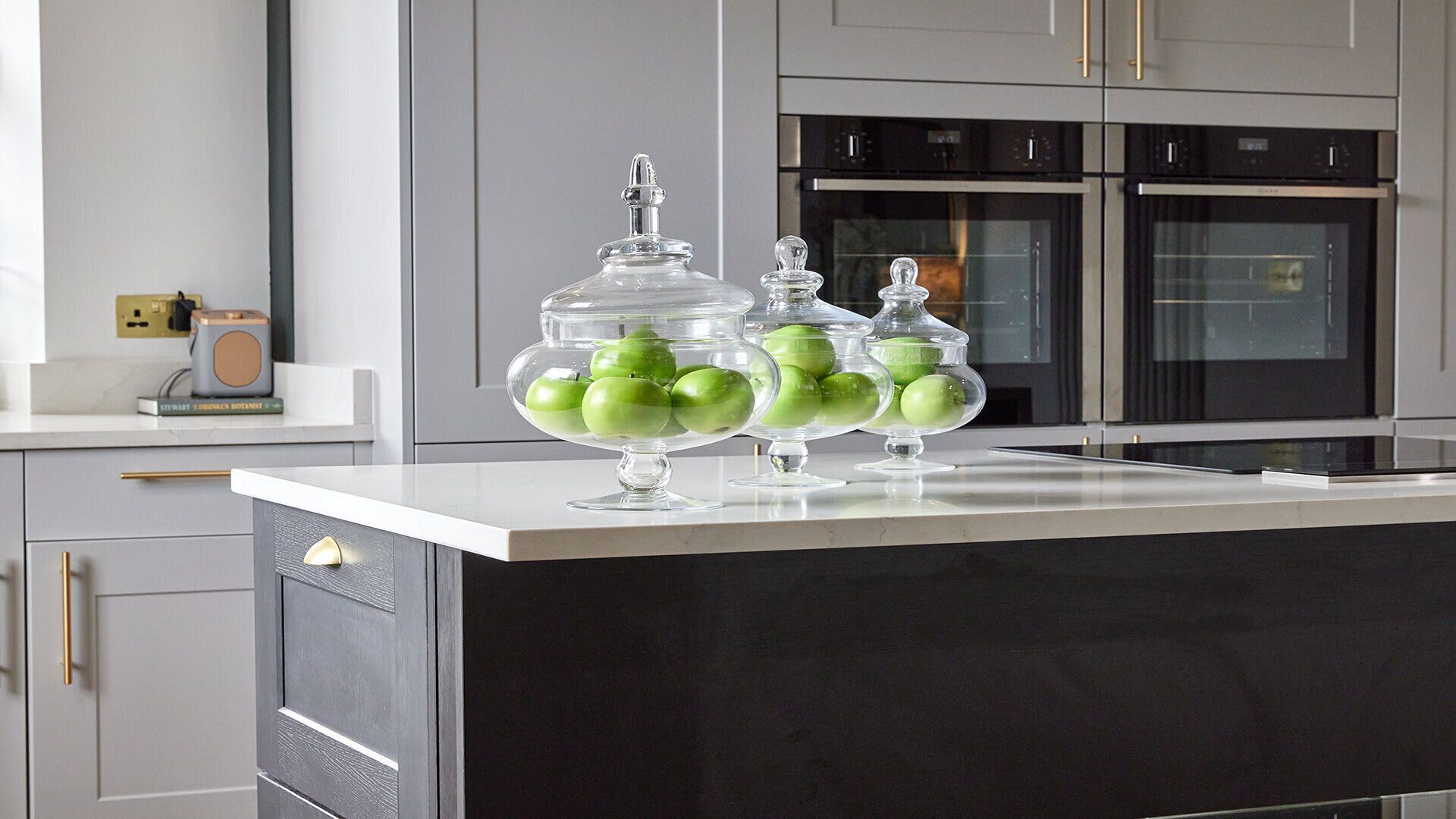 A kitchen with a black countertop, two glass jars with green apples, and modern appliances.