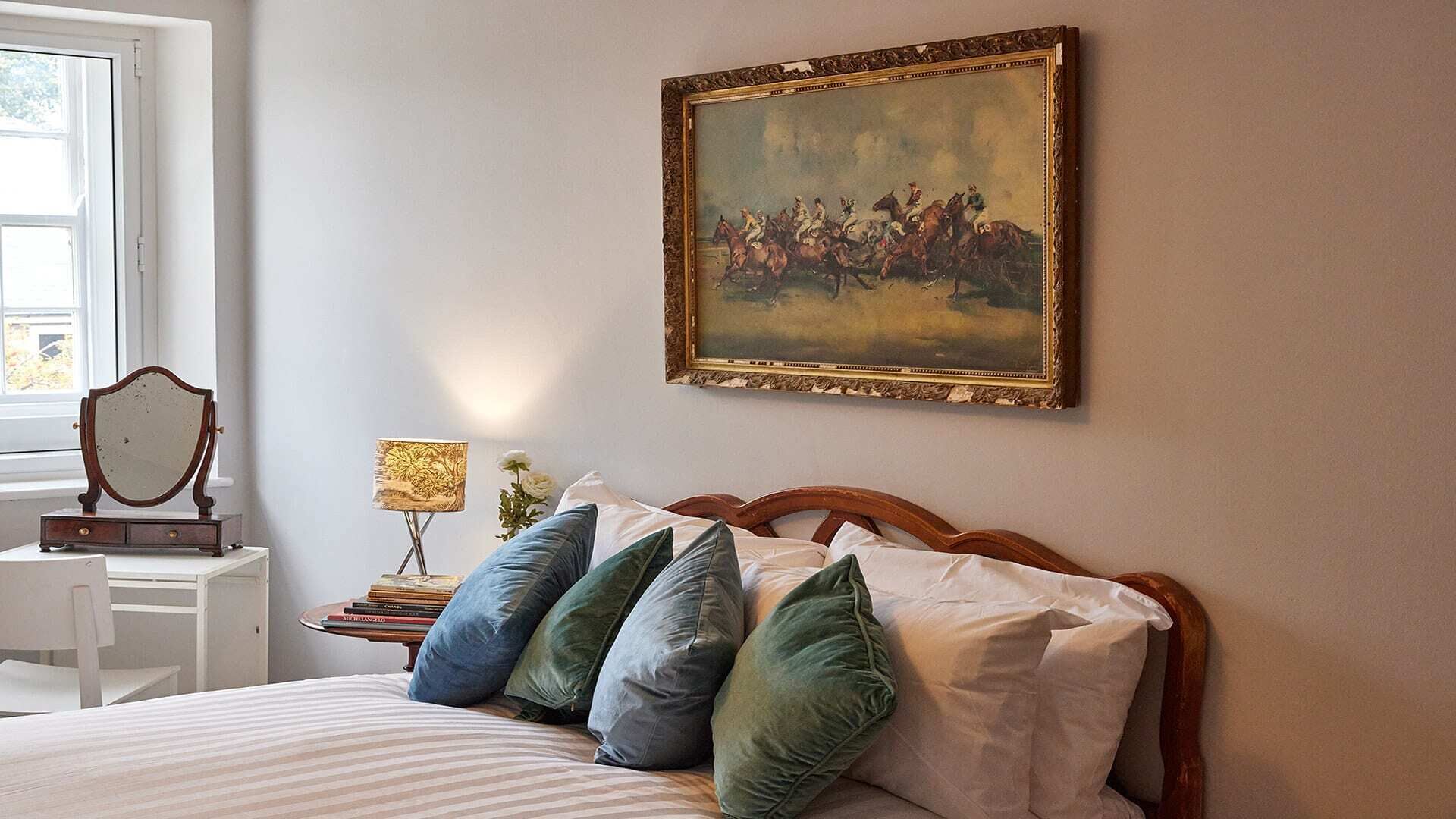 Une chambre à coucher avec un lit, une table de chevet, une lampe, un miroir et un tableau accroché au mur.
