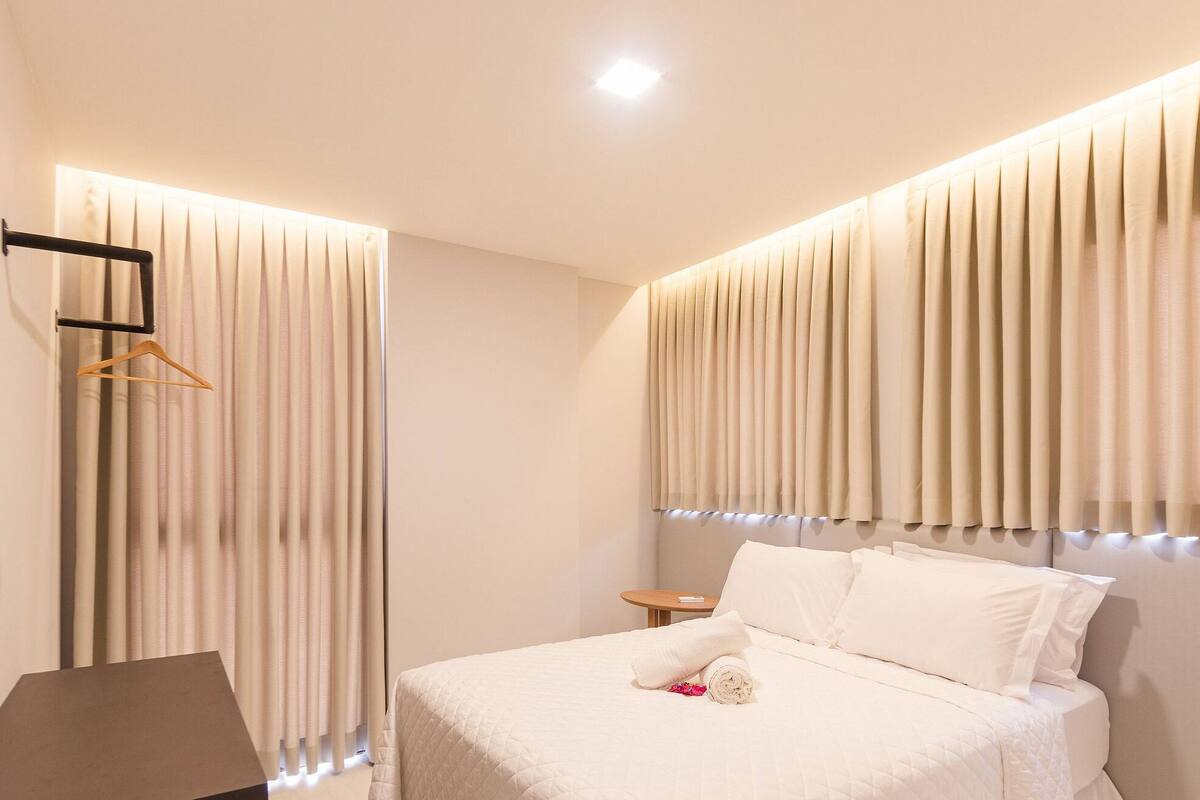 Une chambre d’hôtel moderne avec un lit bien fait, un porte-manteau et une petite table de chevet.