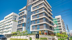 A multi-story hotel with a modern design, featuring balconies and a prominent logo. - Qavi - Gaudium Apart Hotel (João Pessoa)