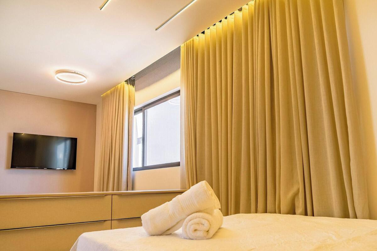 Une chambre d’hôtel avec un lit, un téléviseur à écran plat fixé au mur et une fenêtre avec des rideaux.