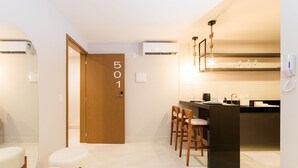 A modern kitchen with a bar area, a wooden door with the number 501, and a phone on the wall. - Qavi - Gaudium Apart Hotel (João Pessoa)