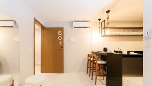 A modern kitchen with a wooden door marked "501", a bar area with stools, and built-in air conditioning units. - Qavi - Gaudium Apart Hotel (João Pessoa)