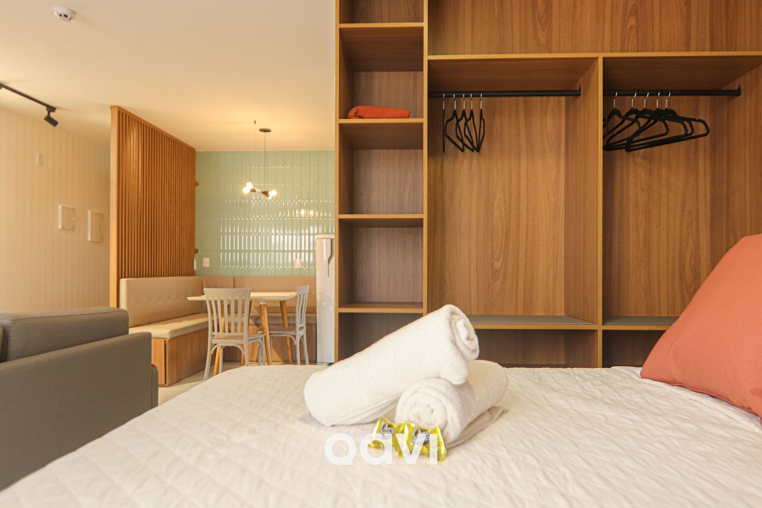 A modern hotel room with a neatly made bed, a wooden wardrobe, a seating area with a table, and a view of the outside.