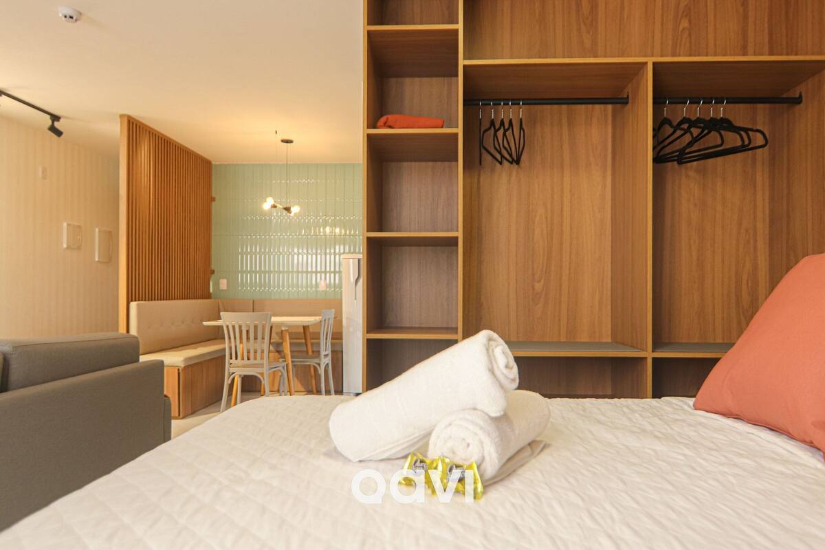 Une chambre d’hôtel moderne avec un lit bien fait, une armoire en bois, un coin salon avec une table et une vue sur l’extérieur.