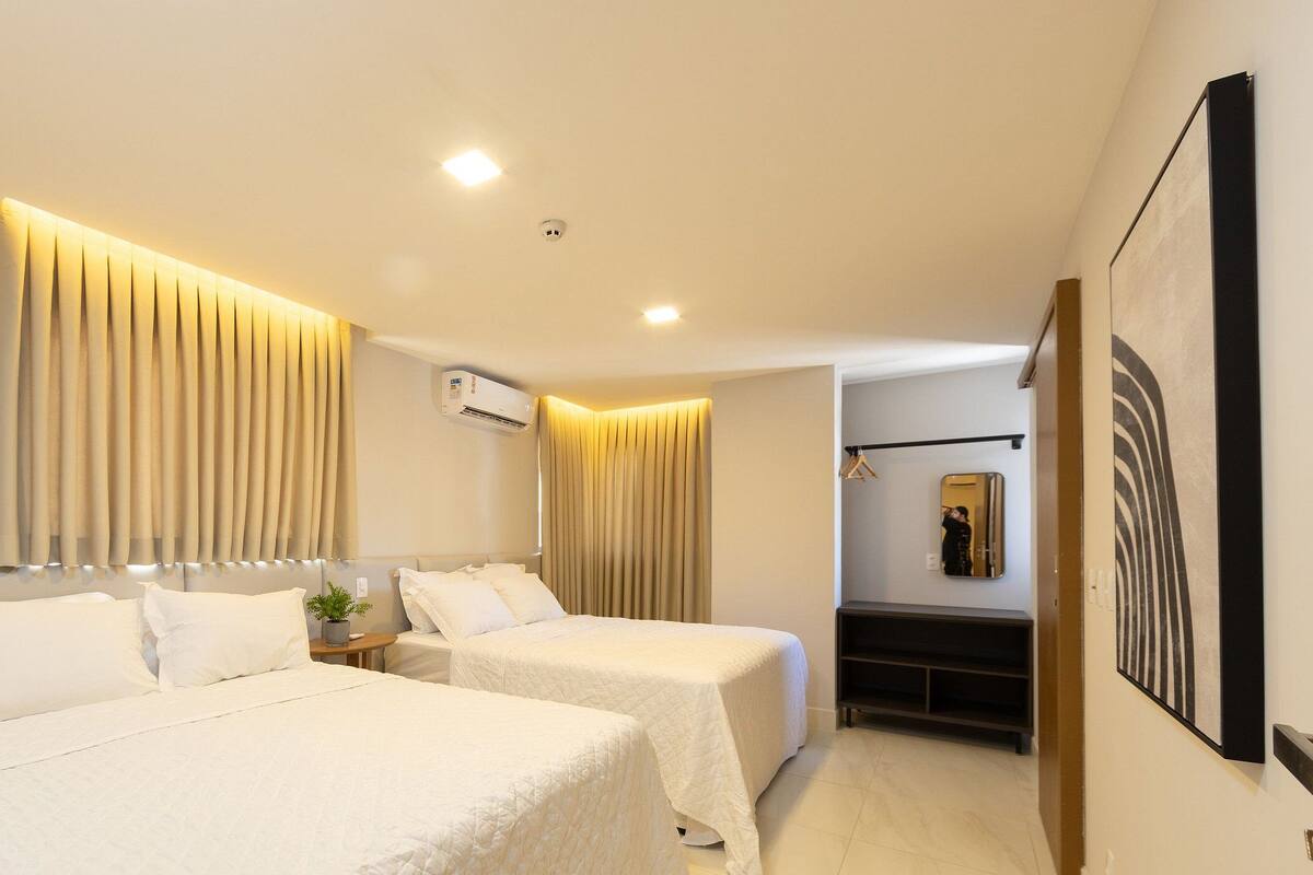 Une chambre d’hôtel avec deux lits, une table de chevet, un appareil de climatisation, un miroir et un tableau au mur.