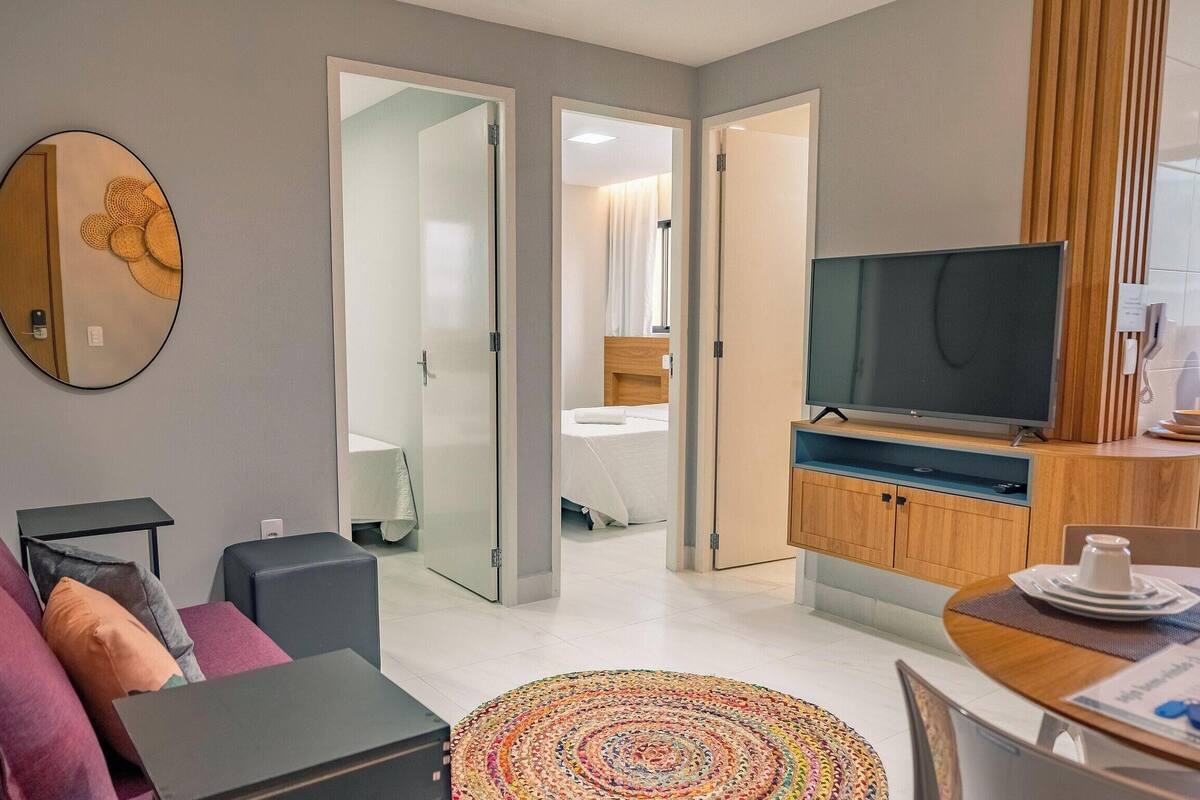 Une chambre d’hôtel moderne équipée d’un canapé, d’une télévision, d’un coin repas et d’une salle de bain visible à travers une porte ouverte.