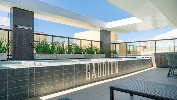 A modern outdoor pool area with a tiled wall labeled "GAUDIUM" and a clear view of the sky. - Qavi - Gaudium Apart Hotel (João Pessoa)