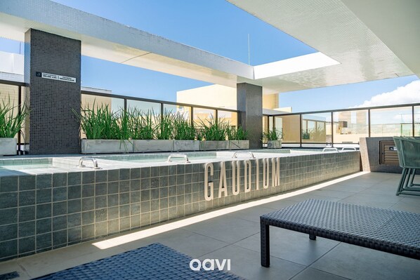 A modern outdoor pool area with a tiled wall labeled "GAUDIUM" and a clear view of the sky. - Qavi - Gaudium Apart Hotel (João Pessoa)