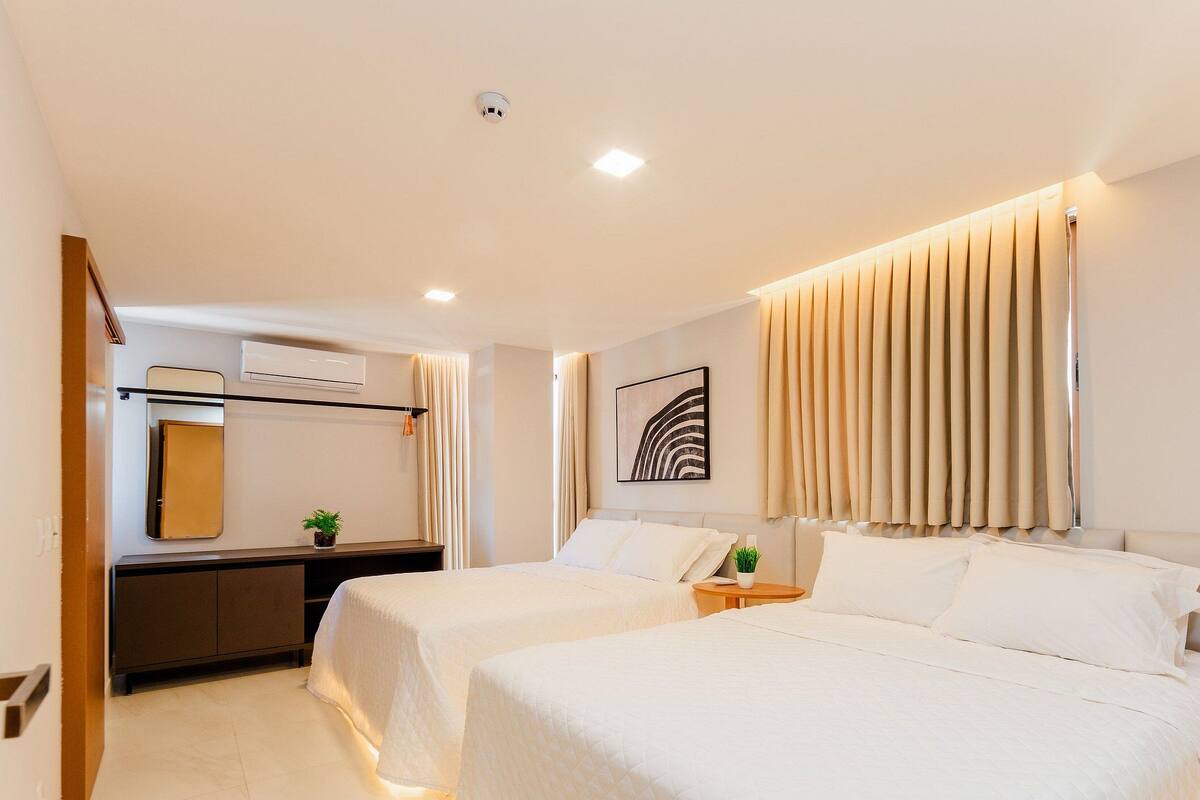 Une chambre d’hôtel avec deux lits, un bureau, un miroir, un appareil de climatisation et une fenêtre avec des rideaux.