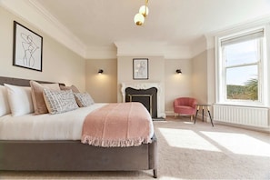 A bedroom with a large bed, a fireplace, a red armchair, and a window with a view. - Host Stay The Old Rectory (Durham)