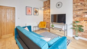 A modern living room with a blue sofa, a yellow armchair, a TV, and a brick wall. - Host Stay Anchor Apartment North Marine House (Scarborough)