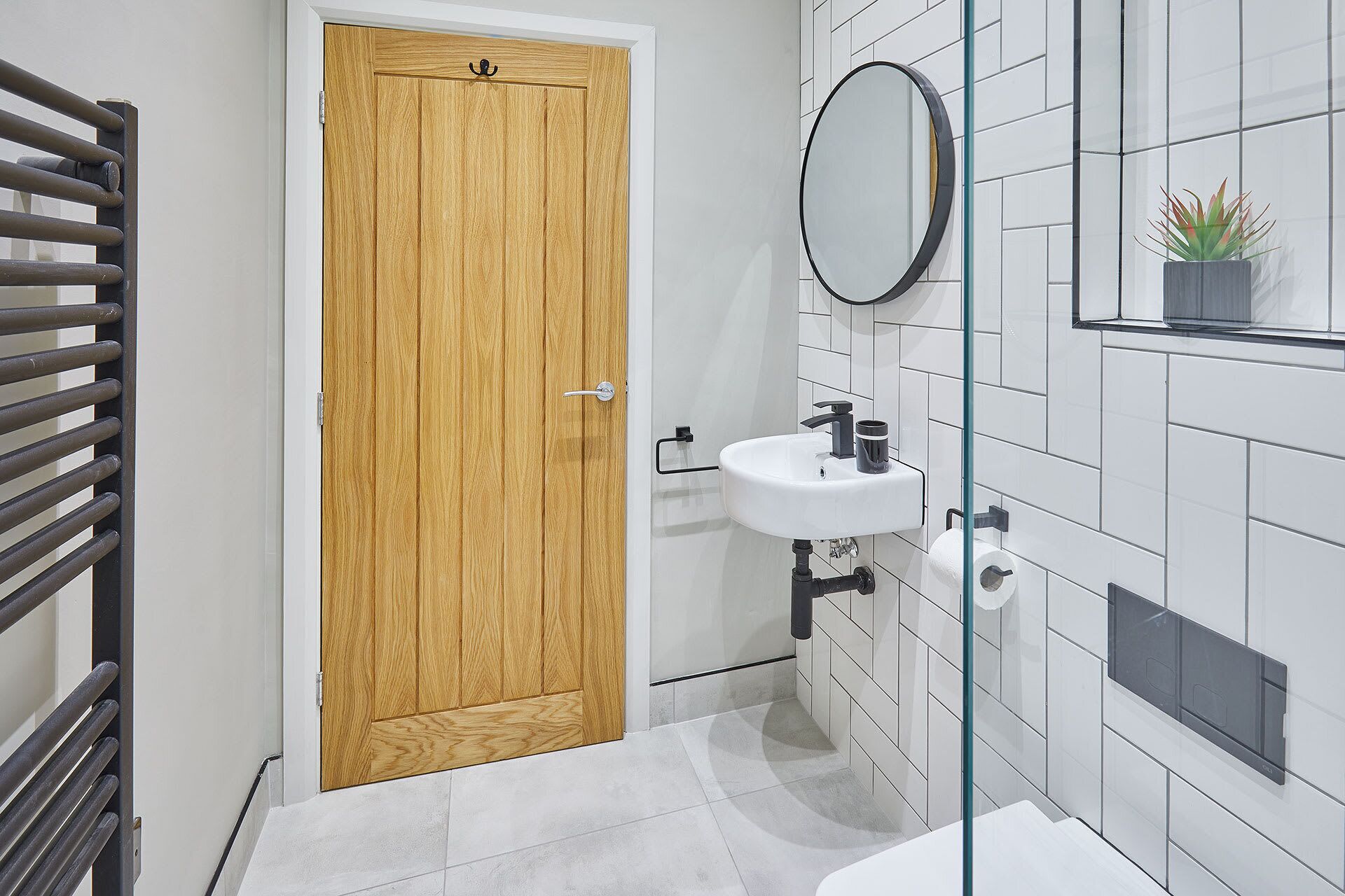 Un baño con puerta de madera, un lavabo blanco con espejo y una planta en maceta en la pared.