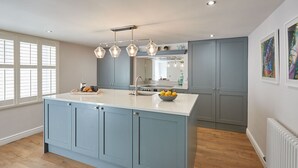 A modern kitchen with a central island, a built-in oven, and a large window with blinds. - Host Stay Devereux House (Whitby)