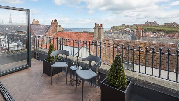 A balcony with a view of a historic castle, terracotta rooftops, and a distant church spire. - Host Stay Devereux House (Whitby)