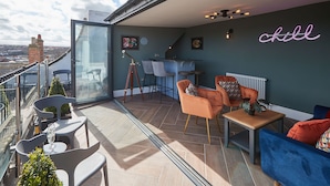A balcony with a glass door, a telescope, and a bar area with chairs and a neon sign. - Host Stay Devereux House (Whitby)