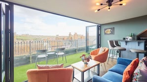 A modern living room with a large glass door leading to a balcony with a view of a cityscape. - Host Stay Devereux House (Whitby)