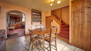 A dining area with a wooden table and chairs, a kitchen in the background, and a wooden staircase. - Host Stay The Red Brick Barn (Bishop Auckland)